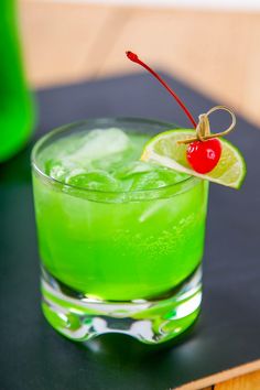 a green drink with a cherry garnish on the rim and a slice of lime