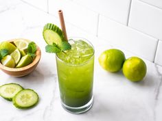 a green drink with cucumber and mint on the side, next to some sliced limes