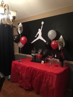 a red table topped with black and white balloons next to a wall mounted air jordan sign