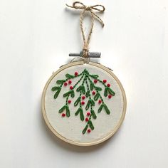 an embroidered christmas ornament hanging from a string on a white surface with red berries and green leaves