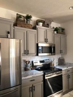 a kitchen with stainless steel appliances and marble counter tops, white walls and gray cabinets