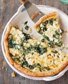 a pizza with spinach and cheese is cut in half on a plate next to a fork