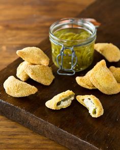 small pieces of breaded food on a wooden cutting board next to a jar of pickle relish