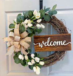 a welcome sign is attached to a wreath on the front door with white flowers and greenery