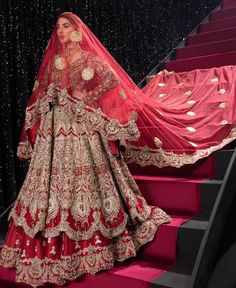 a woman in a red and gold bridal gown standing on stairs with her veil draped over her head