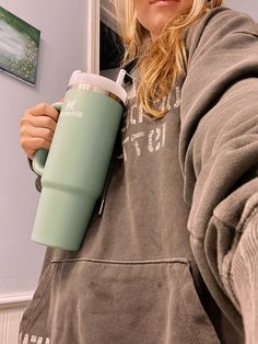 a woman is holding a coffee cup in her hand and looking at the camera while wearing a hoodie