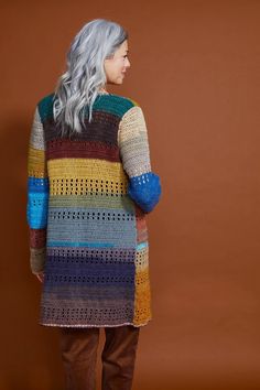 a woman standing in front of a brown wall wearing a multicolored crocheted sweater