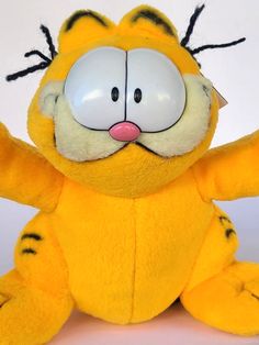 a yellow stuffed animal with its arms out and eyes wide open, sitting on a white surface