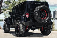 a black jeep with red rims parked by the water