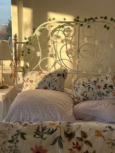 a white iron bed with floral sheets and pillows on it, in front of a window