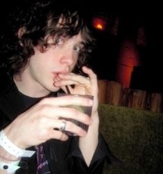 a young man sitting on top of a green couch holding a drink in his hand