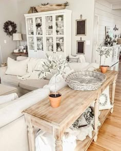 a living room filled with white furniture and lots of plants on top of a wooden table