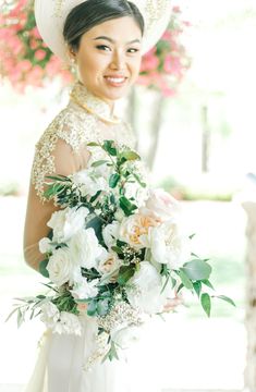 a woman in a white dress holding a bouquet of flowers and wearing a large hat