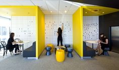 two women are sitting at tables in an office with yellow and black accents on the walls