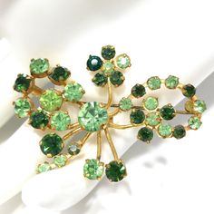 *Description: This is a beautiful green rhinestone brooch, made in Austria, from the 1950s. The rhinestones are in two shades of green; peridot green and emerald green, on a gold tone background. All of the Austrian brooches have exquisite rhinestones. This would be a great addition to your vintage jewelry collection or make a great vintage gift! *Approximate Measurements: Length - 1 1/2 Inches, Width - 2 1/8 Inches, Weight - .3 Ounce *Condition: Great vintage condition. Pin in clasp is brass an