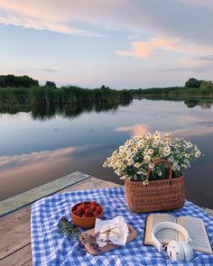 a picnic table with food and flowers on it next to the water at sunset or dawn