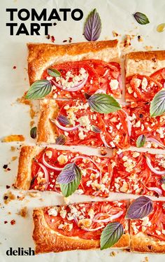 an overhead view of a pizza with tomatoes and herbs on it, cut into squares