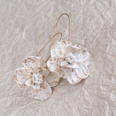 Description Looking for a unique piece? These white flower speckled gold earrings are handmade, lightweight, and jaw-dropping. Gold leaf is hand pressed into each petal for just the right amount of sparkle. These make for a fantastic bridesmaid proposal gift. Details Extremely lightweight Hand pressed gold leaf Hand sculpted from polymer clay Nickel-free Durable Shipping 2-3 weeks During busy seasons, orders of 6 or more pieces may incur a longer turnaround of 4+ weeks; please remember to order White 14k Gold Filled Bridal Earrings As Gift, 14k Gold Filled White Bridal Earrings As Gift, Delicate White 14k Gold Filled Earrings, Delicate Handmade Earrings For Bridesmaids, White 14k Gold Filled Earrings For Weddings, White 14k Gold Filled Bridal Earrings For Wedding, Delicate Gold Flower Earrings With Handmade Flowers, Delicate Gold Flower Earrings With Handmade Details, Gold Bridal Earrings With Handmade Flowers