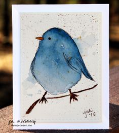 a blue bird sitting on top of a wooden table next to a white card with watercolor