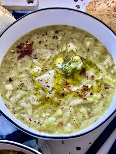 there is a bowl of soup with broccoli in it and bread on the side