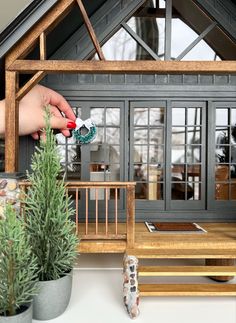 a hand is holding a brush over a doll house with wooden furniture and decorations on the front porch