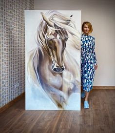 a woman standing next to a painting of a horse