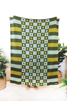 a large green and yellow blanket sitting on top of a white floor next to potted plants