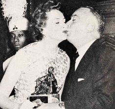 an old black and white photo of a man kissing a woman in front of him