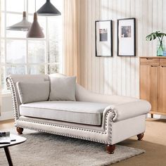 a white chaise lounger in a living room next to a table and lamp