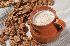 some pecans are scattered around a coffee mug on a wooden table with milk in it