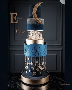 a three tiered cake with blue and gold icing, stars and the moon on top