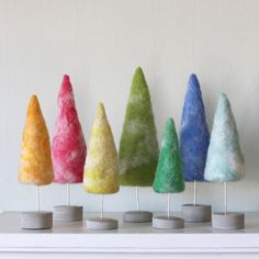 small felted trees are lined up on the mantle in front of a white wall