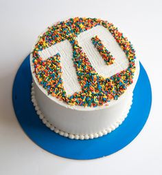 a white cake with sprinkles and the letter d on top is sitting on a blue plate