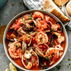 a bowl filled with seafood and clams in tomato sauce next to bread on the side