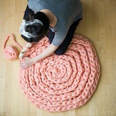 a woman laying on the floor with her dog next to a large knitted rug