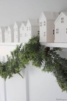 christmas garland hanging on the wall with small white houses and pine cones in front of them