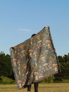 a person standing under a blanket on top of a grass covered field with trees in the background