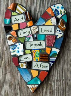 a heart shaped mosaic with words written in different colors and shapes on the inside, sitting on a wooden surface