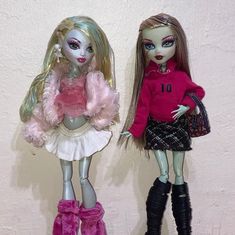 two dolls standing next to each other in front of a white wall with pink and black accents