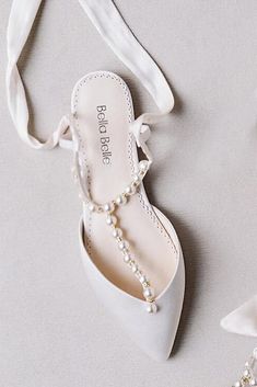 a pair of white shoes with pearls on the side and a ribbon tied around them