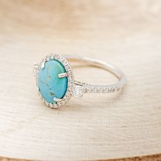 a turquoise stone and diamond ring sitting on top of a wooden table