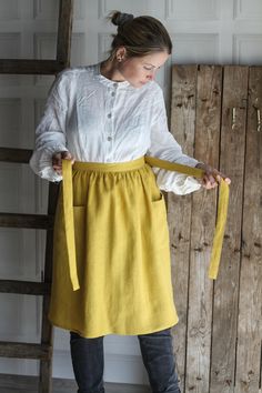 a woman wearing a yellow skirt and white shirt is standing in front of a wooden wall