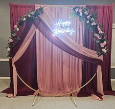 a happy birthday sign is lit up in front of a backdrop with roses and greenery