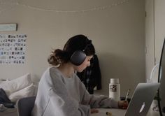 a woman sitting in front of a laptop computer wearing headphones on her ears and looking at the screen