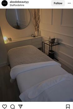 a bed with white sheets and pillows in a bedroom next to a mirror on the wall