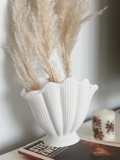 a white vase sitting on top of a table next to a book and candle holder