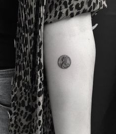 a woman's arm with a small coin tattoo on the left side of her arm