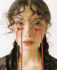 a woman with long hair and red ribbons tied to her face