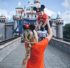 a woman holding a baby up to her face in front of mickey mouse's castle