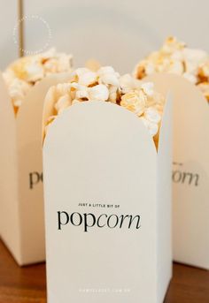 two white popcorn bags sitting on top of a wooden table with the word popcorn printed on them